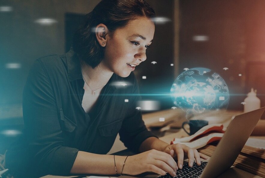 Woman sitting at laptop with hologram of world