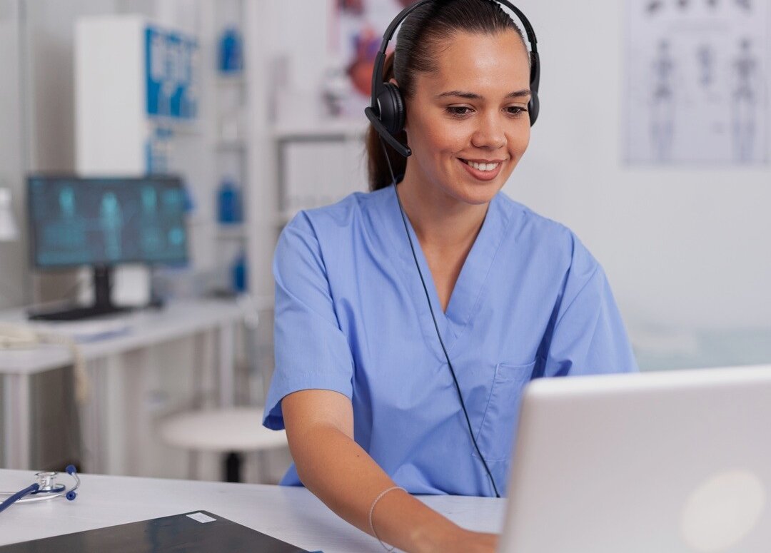 Pflegekraft sitzt an Laptop mit Headset